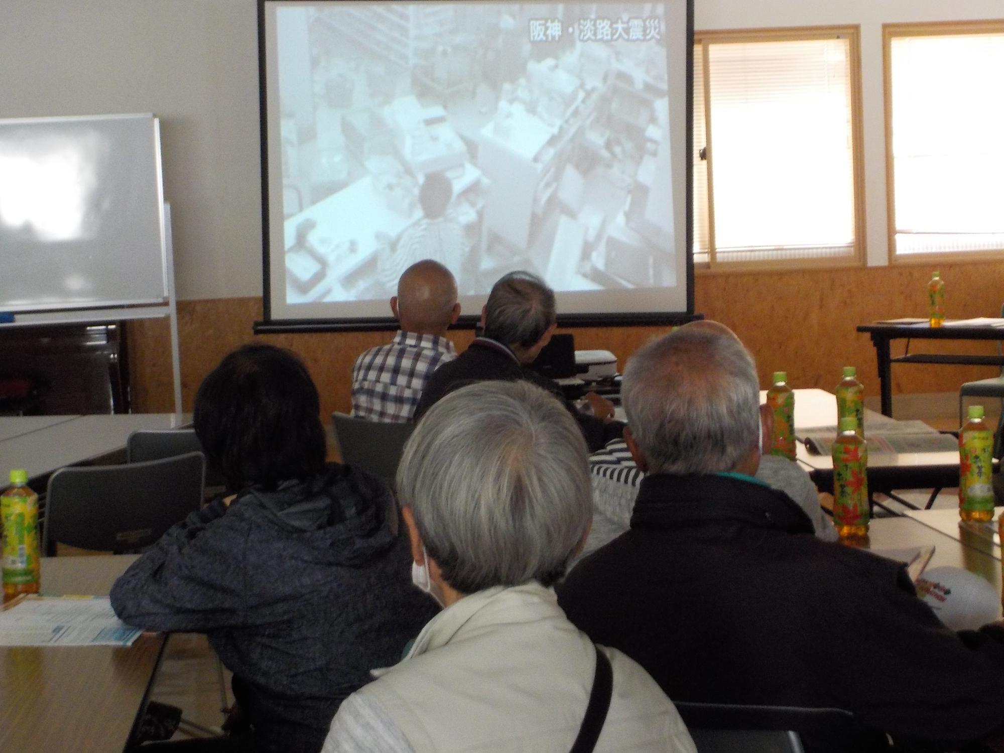 参加者たちが部屋の前の方にあるスクリーンに映し出された映像を観ている写真