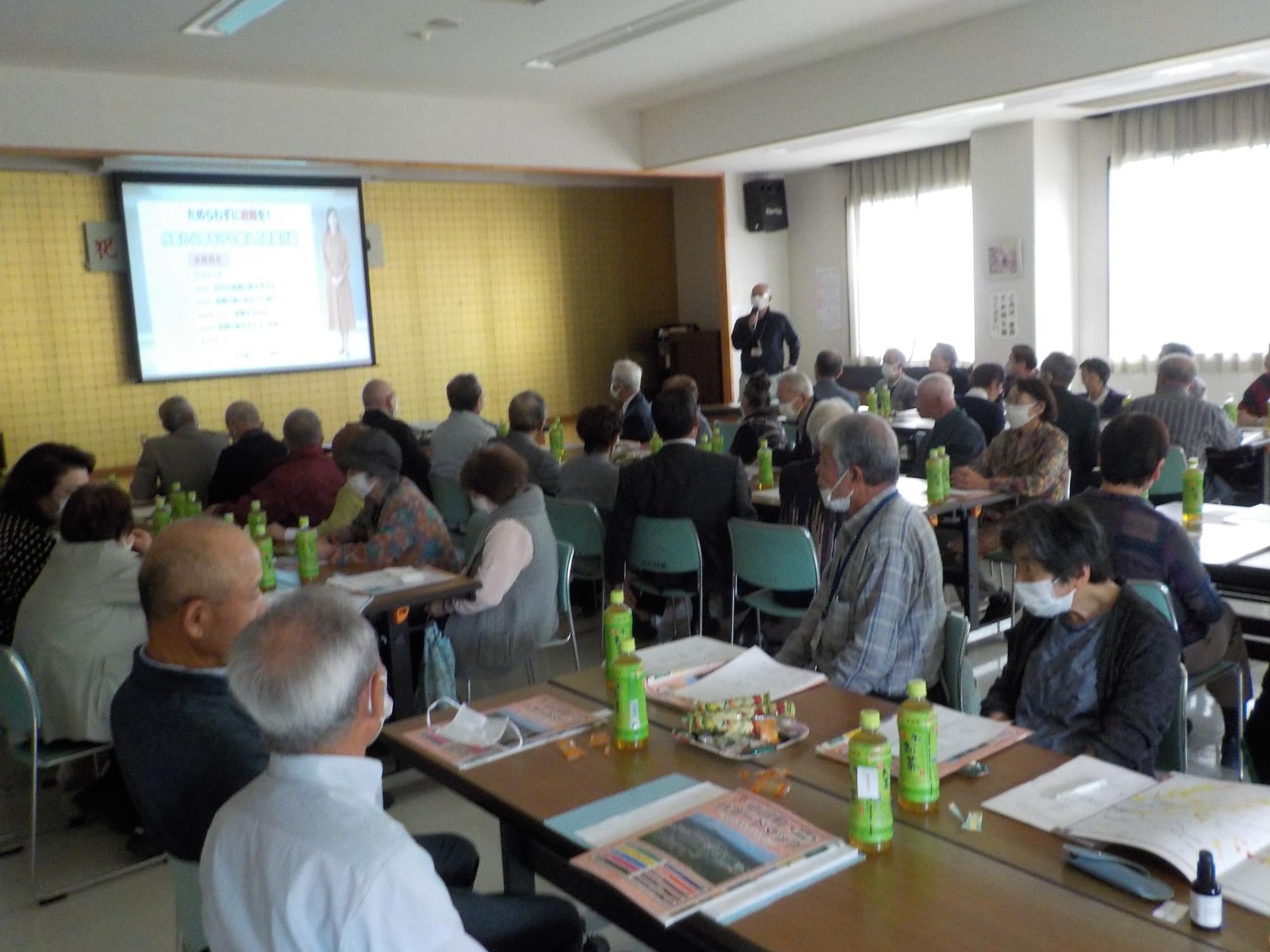 防災講座の参加者たちが、マイクを持った男性の話を聞いている写真