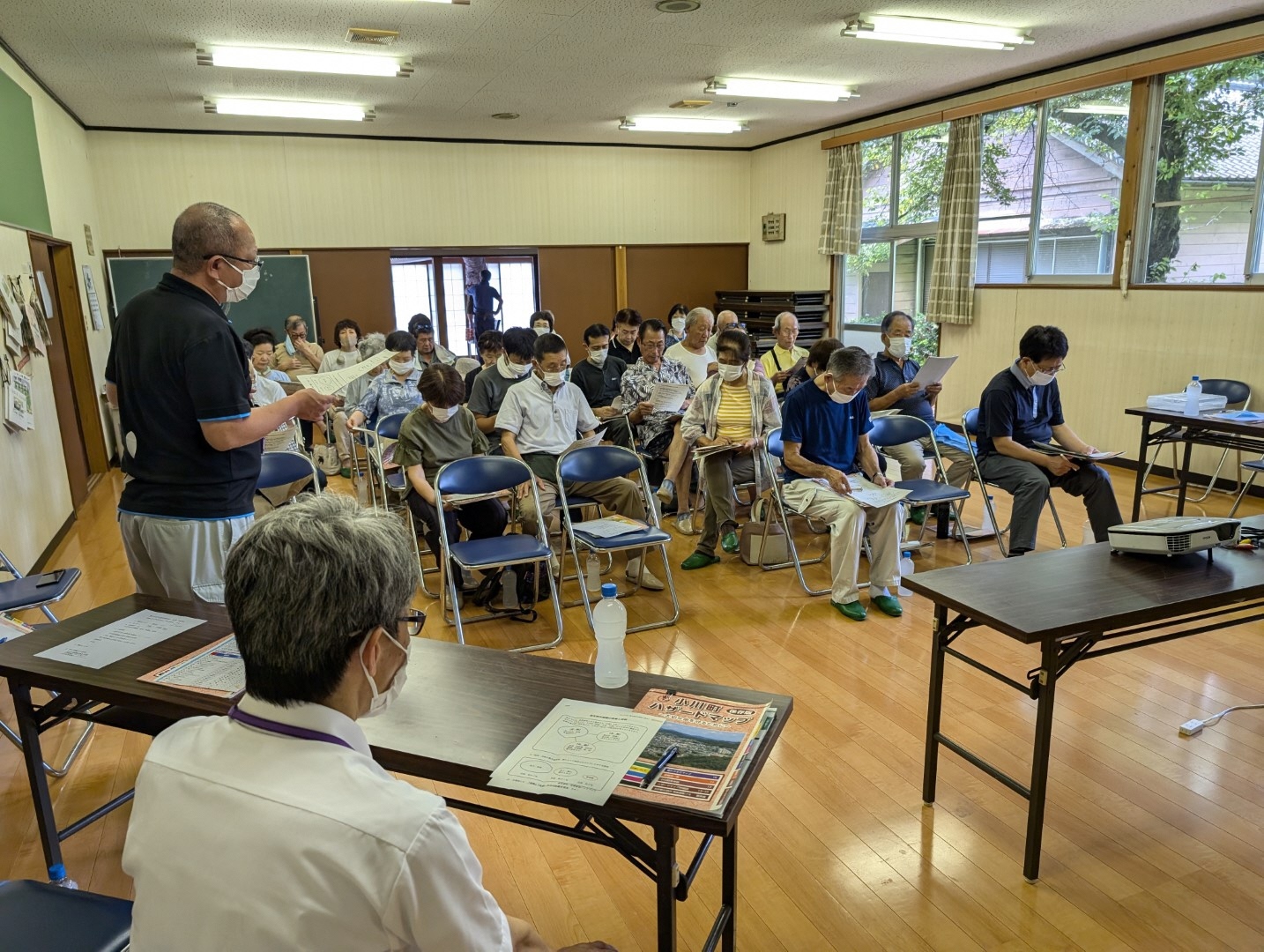 スクリーン側から説明している男性の前に座る多くの受講者の方々が話を聞いている様子を前面から撮影した写真