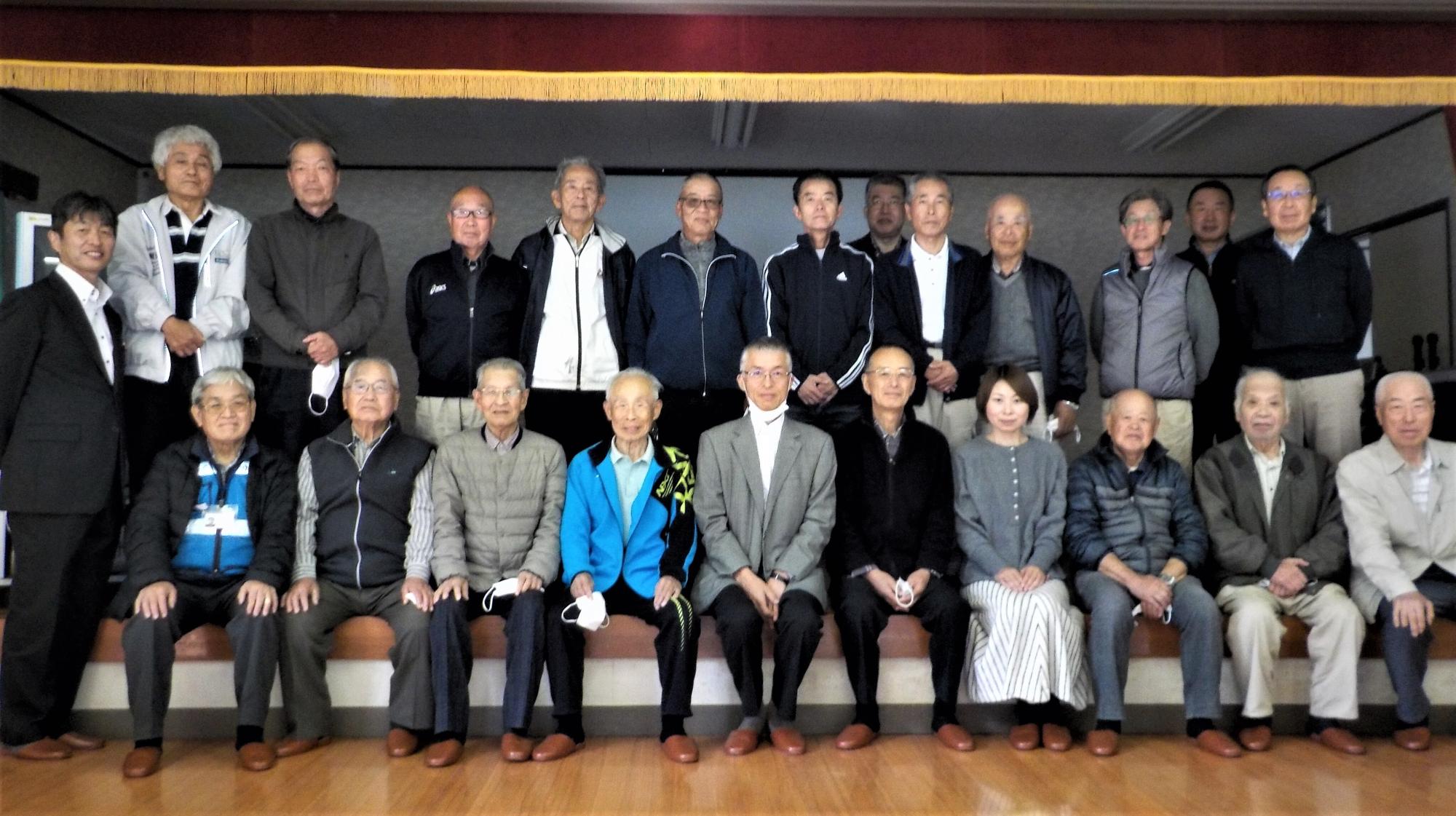 研修会の参加者たちが広い部屋の中で横2列並びに並んで集合している写真