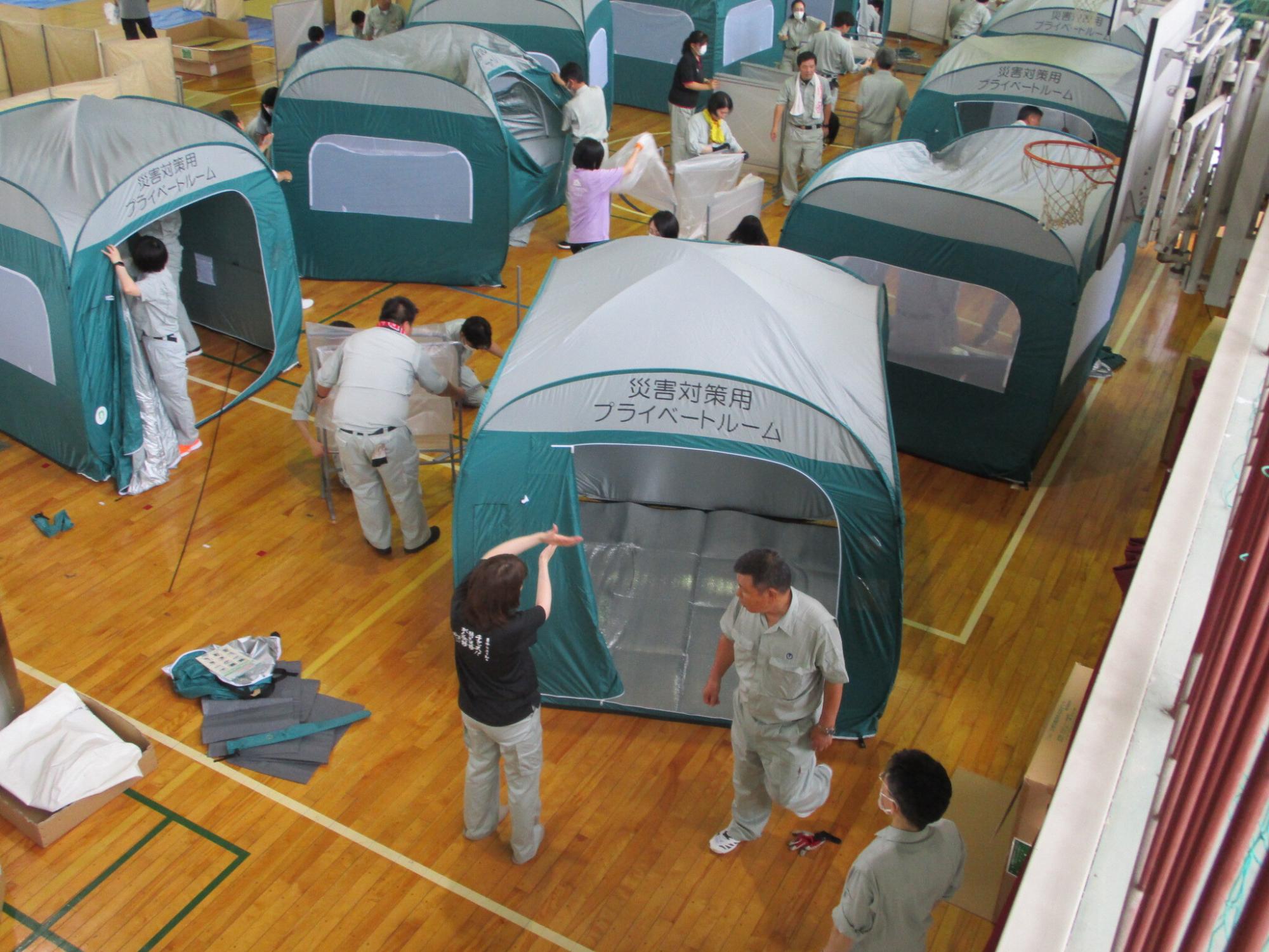 体育館で参加者たちがプライベートルームとして使えるテントを組み立てている写真