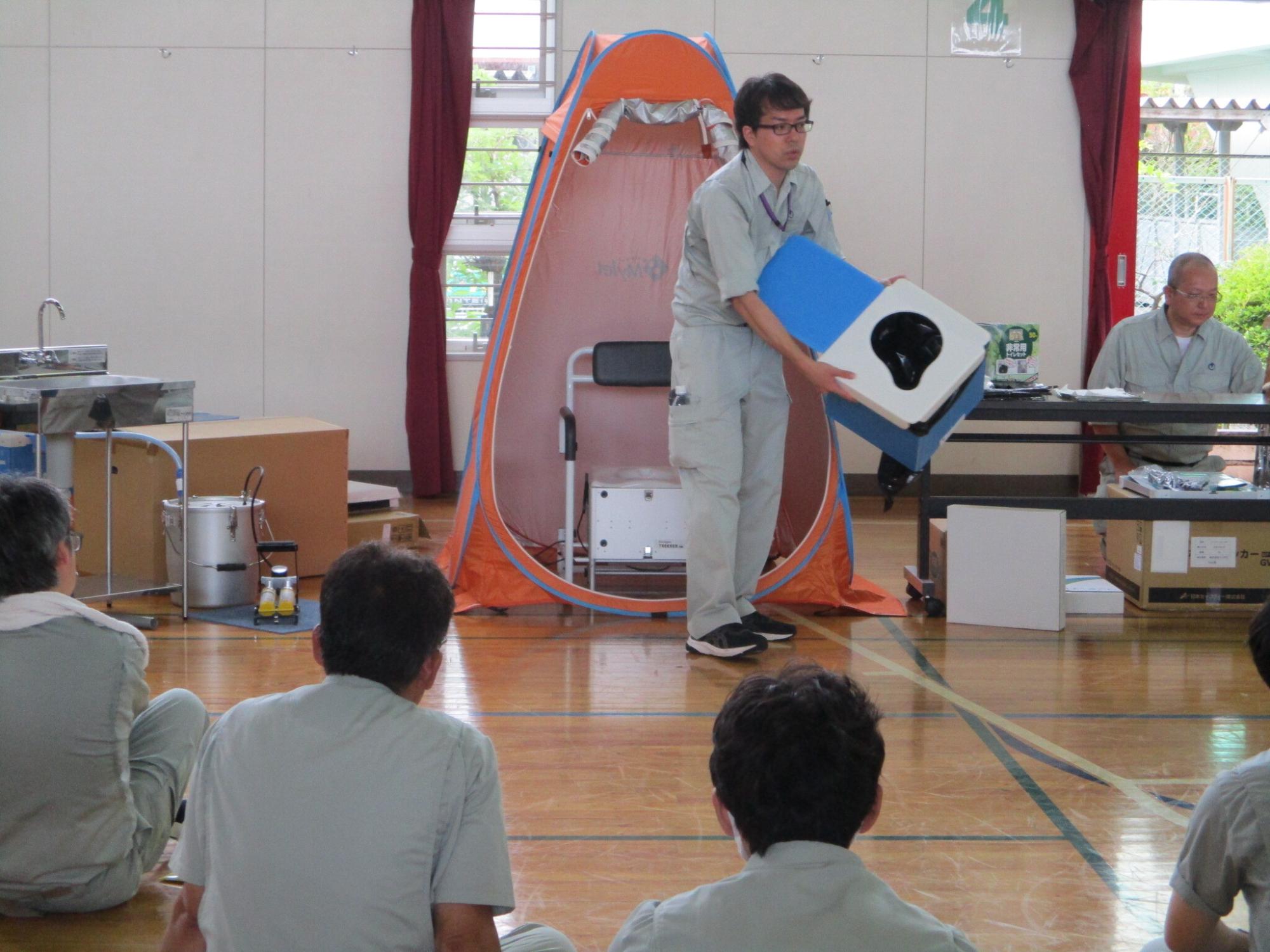 防災用品を手に持った男性が参加者たちの前で話をしている写真