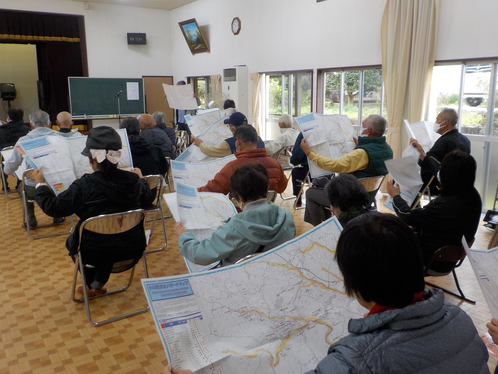 椅子に座った参加者たちがそれぞれハザードマップを広げてマップの内容を確認している写真