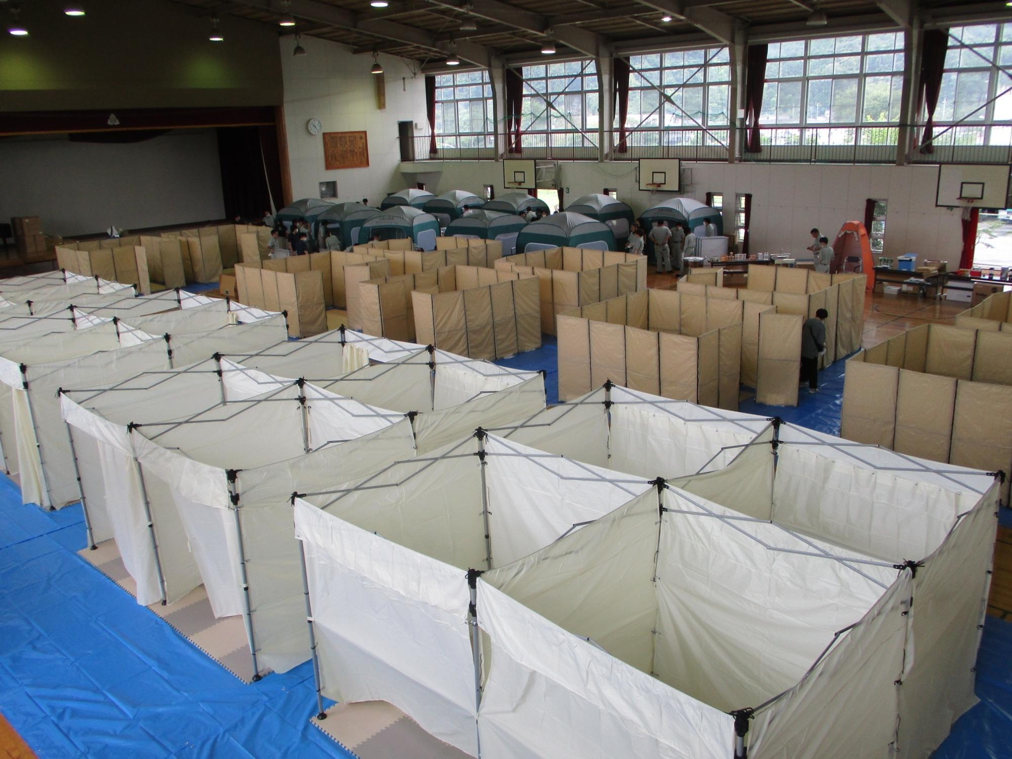 体育館にたくさんの組み立てられた仕切りやテントなどがずらりと置かれている写真