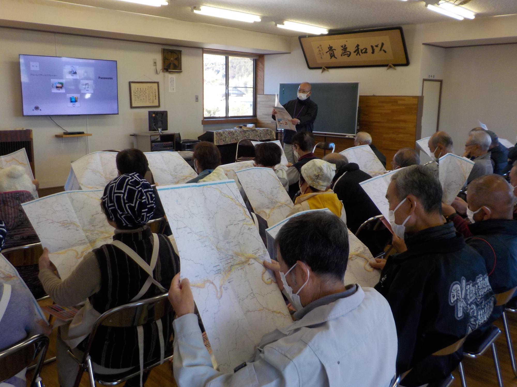 訓練の参加者たちが部屋の中でそれぞれ手に持ったハザードマップを見ている写真