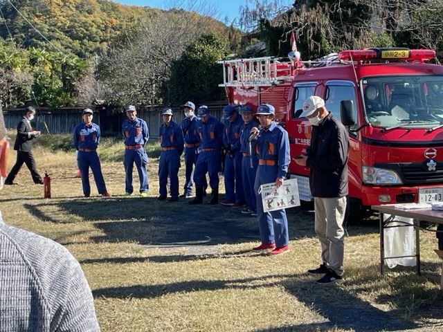 制服を着た消防団の団員が屋外で訓練の参加者たちに話をしている写真