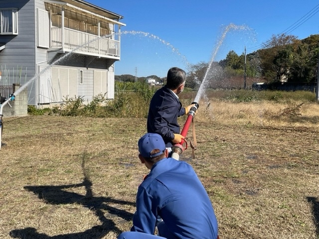訓練の参加者と消防団の団員が大きなホースから勢いよく水を出して放水訓練を行っている写真