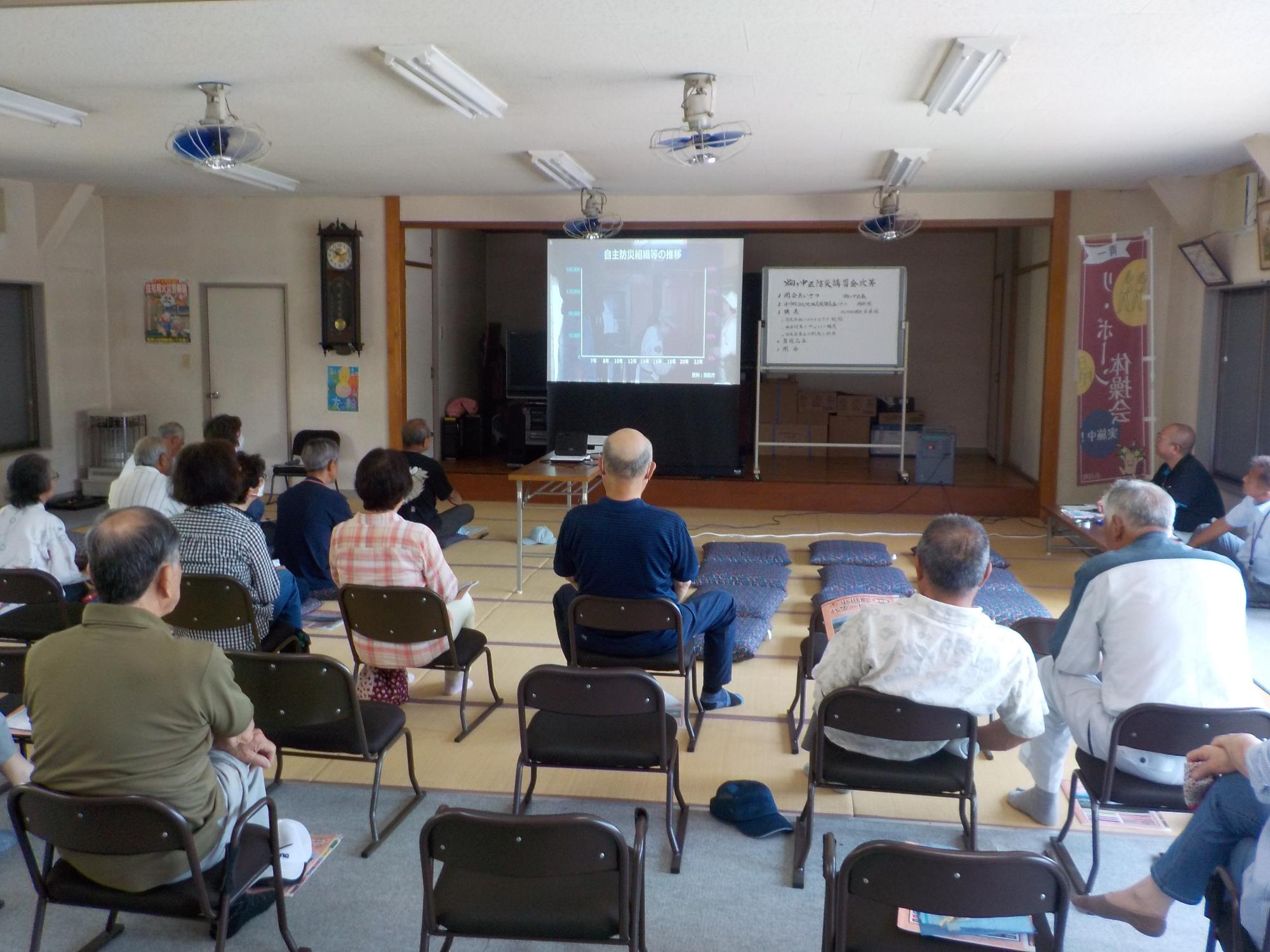 前方のスクリーンに映し出されたDVDの映像を視聴している参加者の方々の後姿を撮影した写真