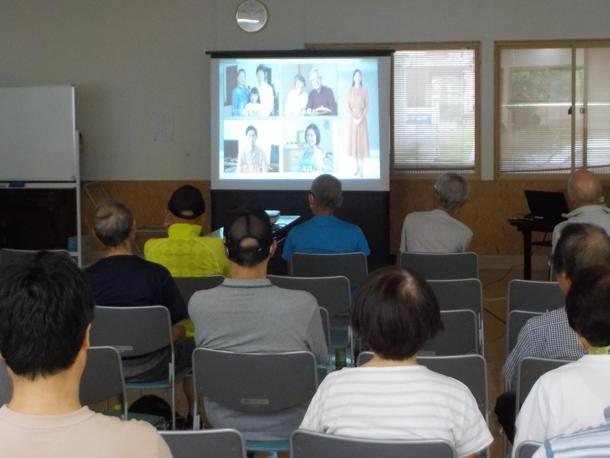 室内前方のスクリーンに映し出された映像を真剣に見ている参加者達の後ろ姿の写真