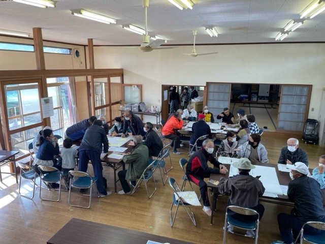 参加者たちが3つのグループに分かれ、大きなテーブルの前の椅子に座りながら互いに避難経路の確認などを行っている写真