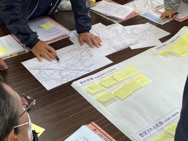 参加者たちが大きなテーブルの上に地図を置いて避難方法の確認と共有を行っている写真