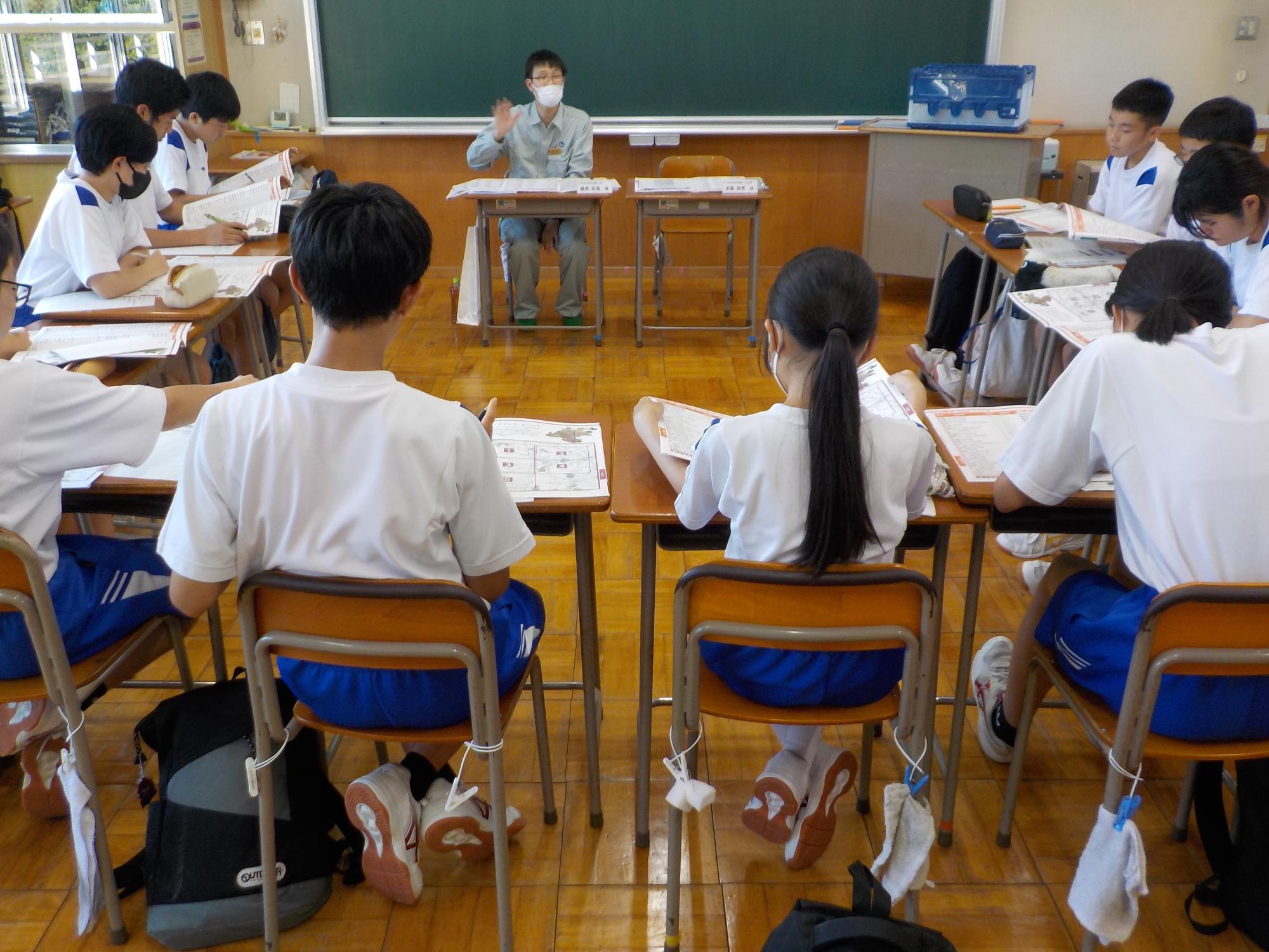 ロの字型に設置した席の前方に職員の方が座り、生徒達が資料を見ながら職員の方の話を聞いている様子の写真