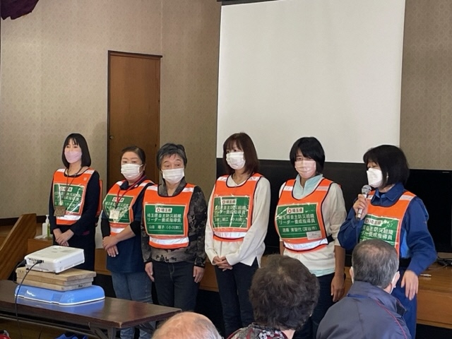 参加者たちが集まる部屋の前方に6人の指導員が横並びに並んで立っている写真