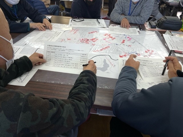 参加者たちが机の上に置かれた大きな地図を前にして話し合いをしている写真