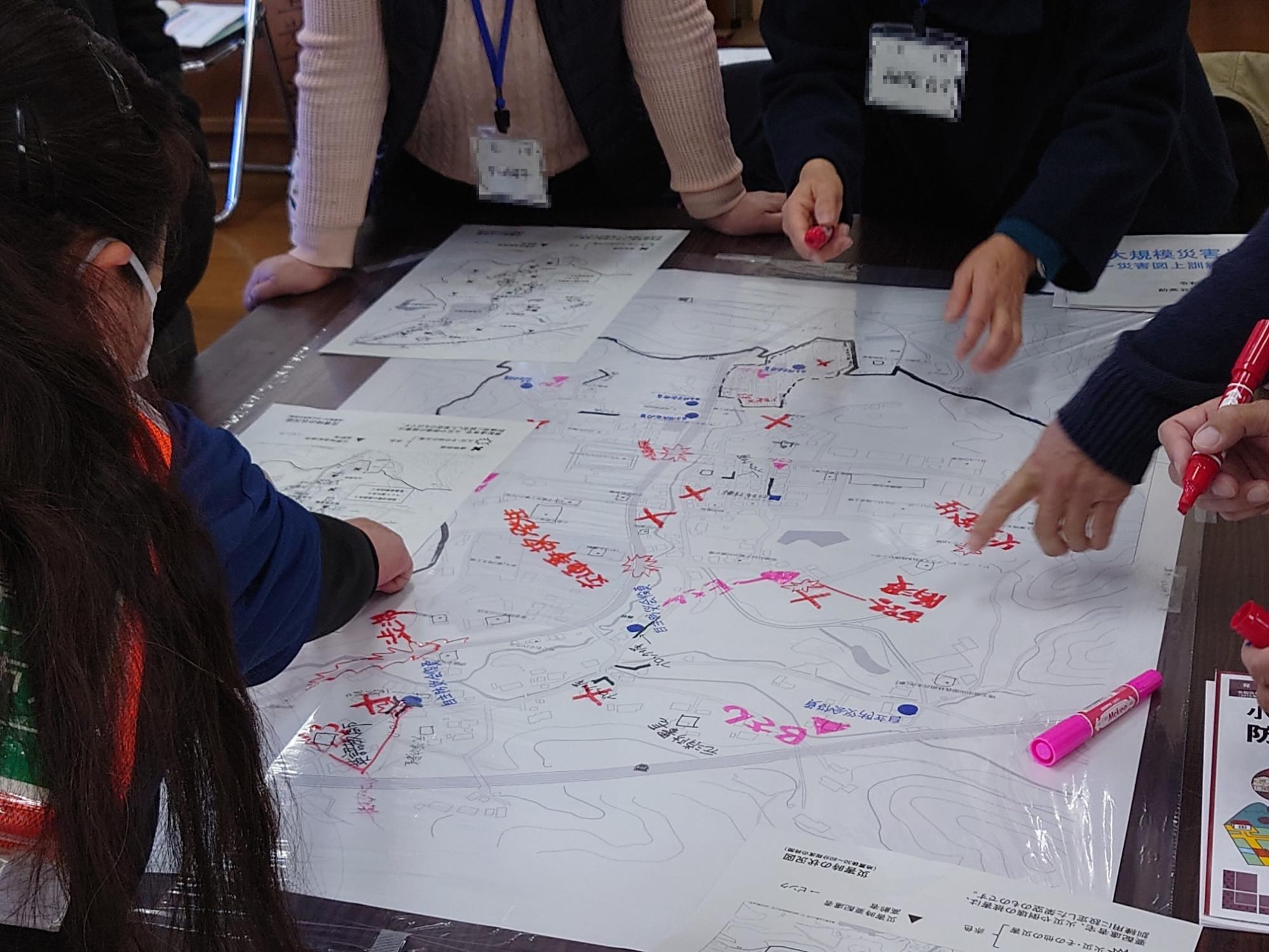 参加者たちが机の上に置かれた大きな地図に印をつけたり文字を書き込んだりして話し合いをしている写真