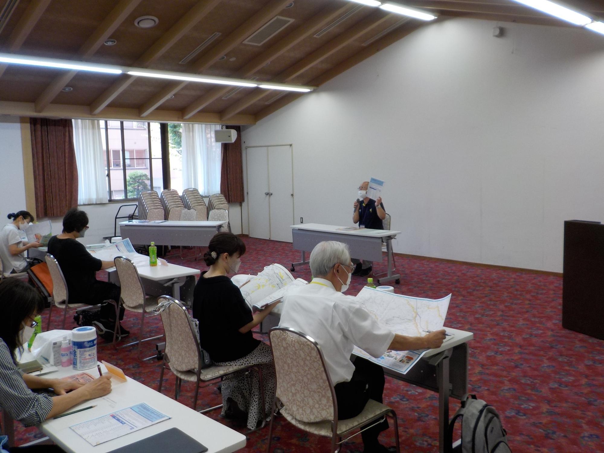 会議室で防災研修を行う男性講師と男性講師の話に耳を傾ける参加者たちの写真