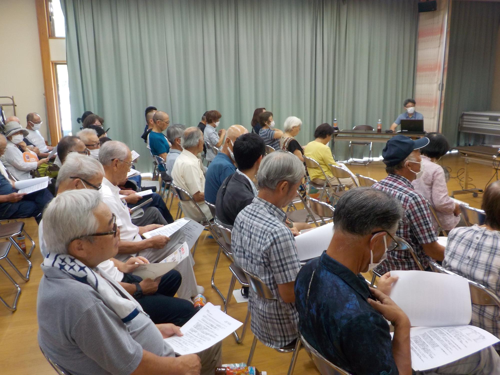 5列に並べられたパイプ椅子に座っている参加者達を横から写した写真