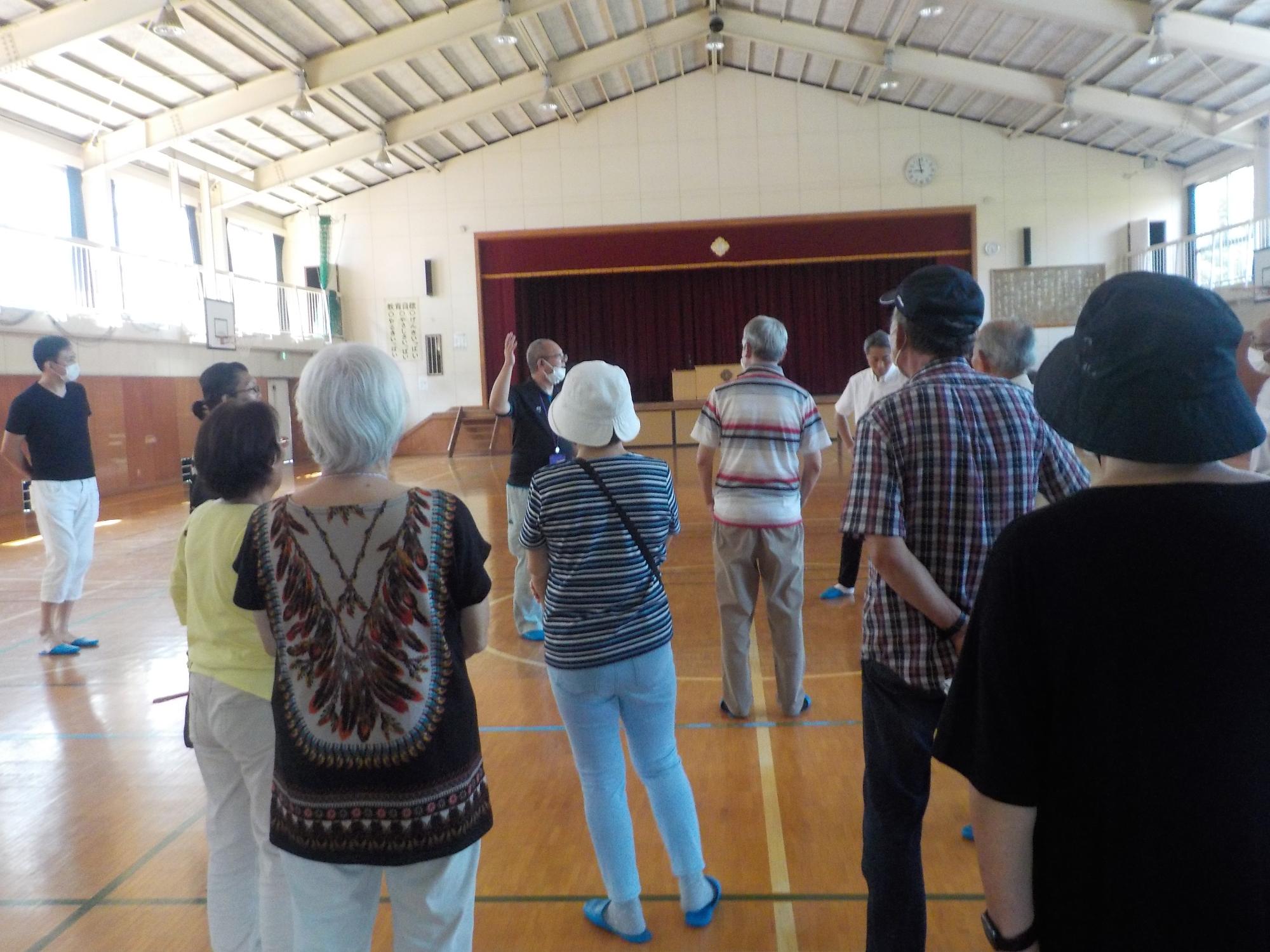 体育館に参加者達が集まり、男性の話を聞いている写真