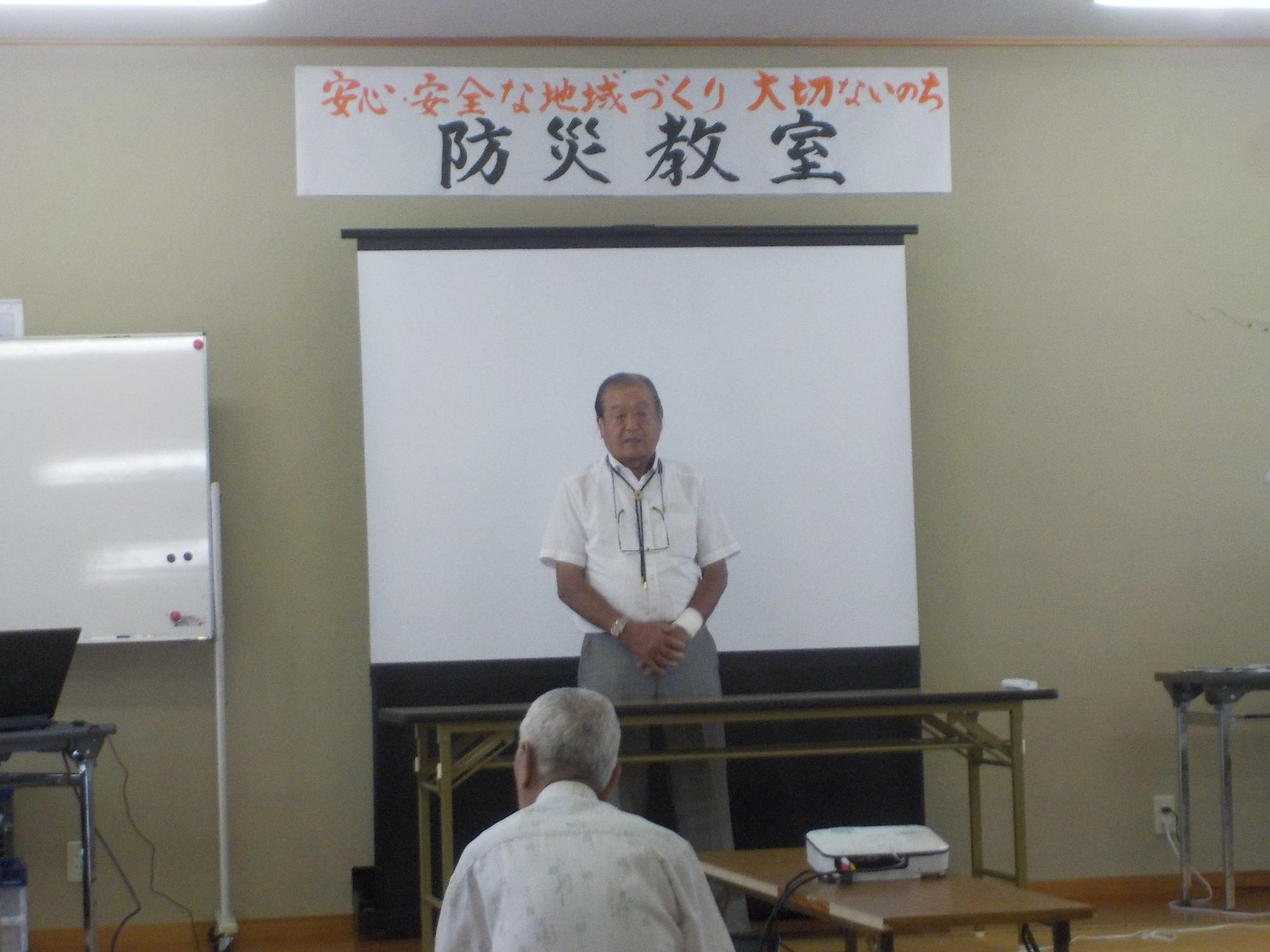 「安心安全な地域づくり 大切ないのち 防災教室」と書かれた紙が壁に貼られている前で、能増区長が立ってあいさつをしている様子の写真