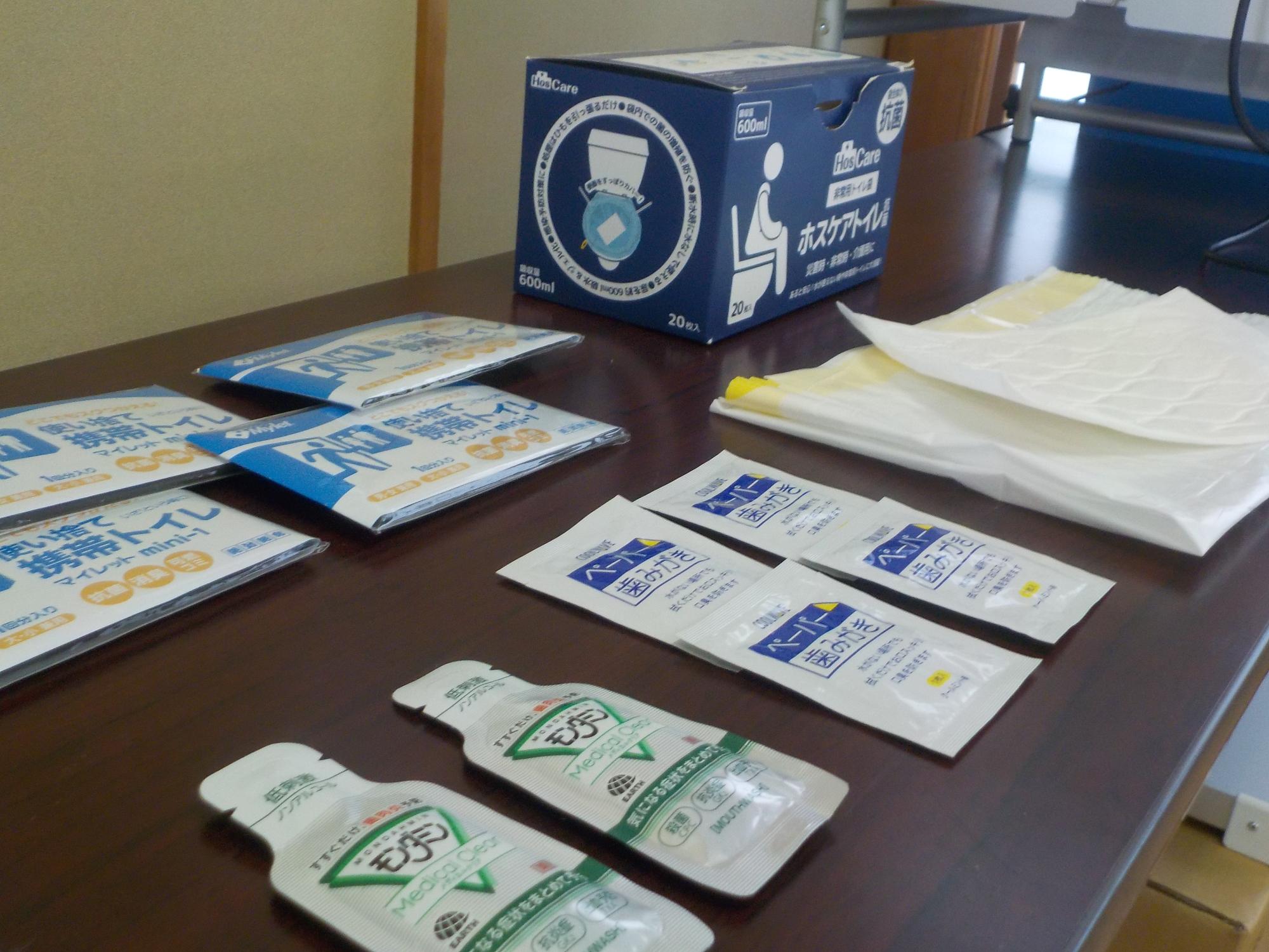 長机の上に並べられている、携帯トイレのパック、ペーパー歯みがき、マウスウォッシュなどの防災グッズの写真