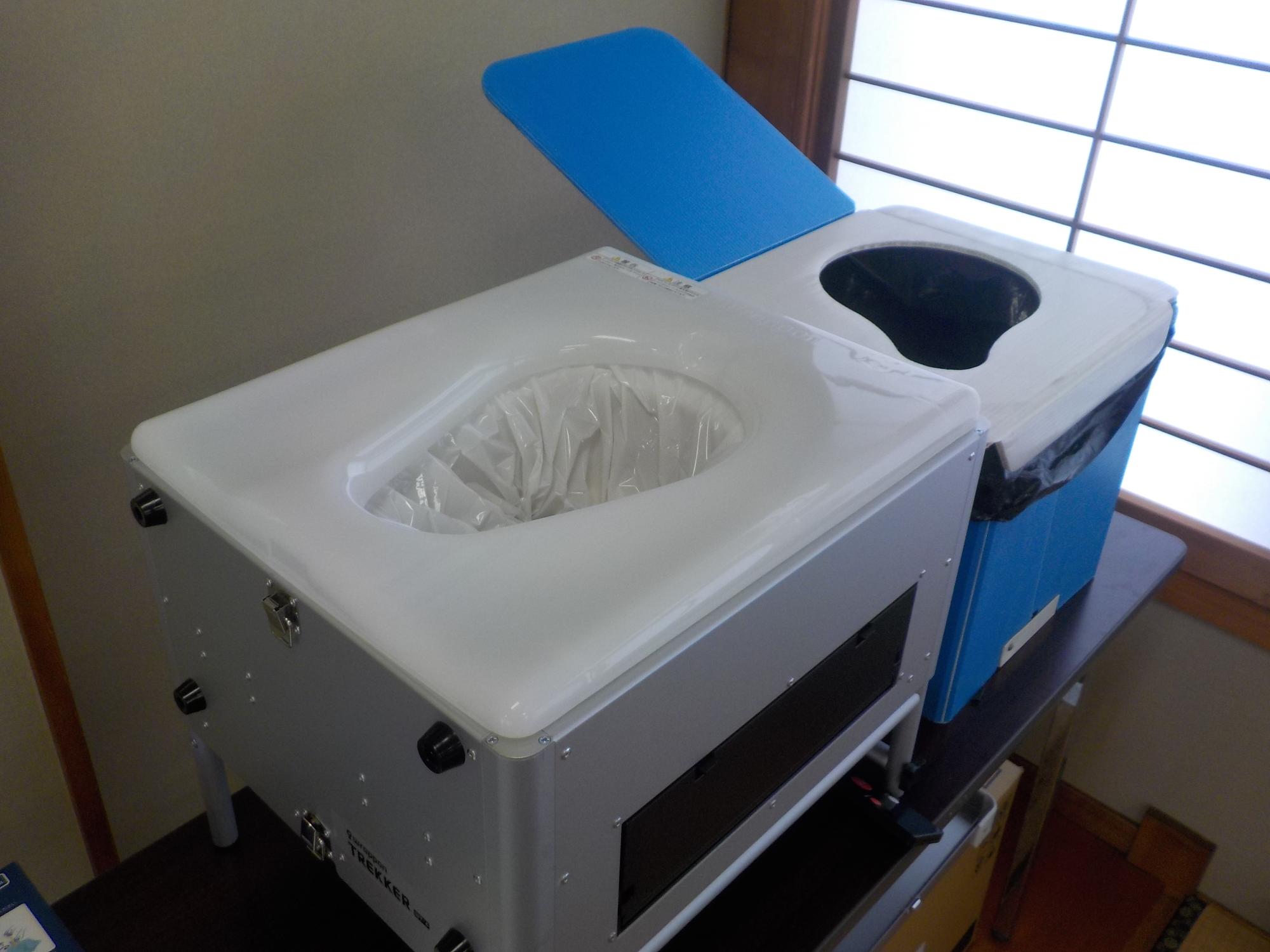 長机の上に置かれている白色と青色の2種類の箱型のトイレの写真