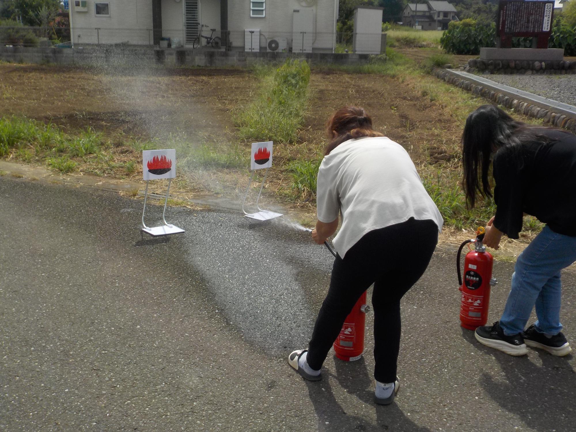 火に見立てた的に向かって2人の女性が水消火器で放水している写真