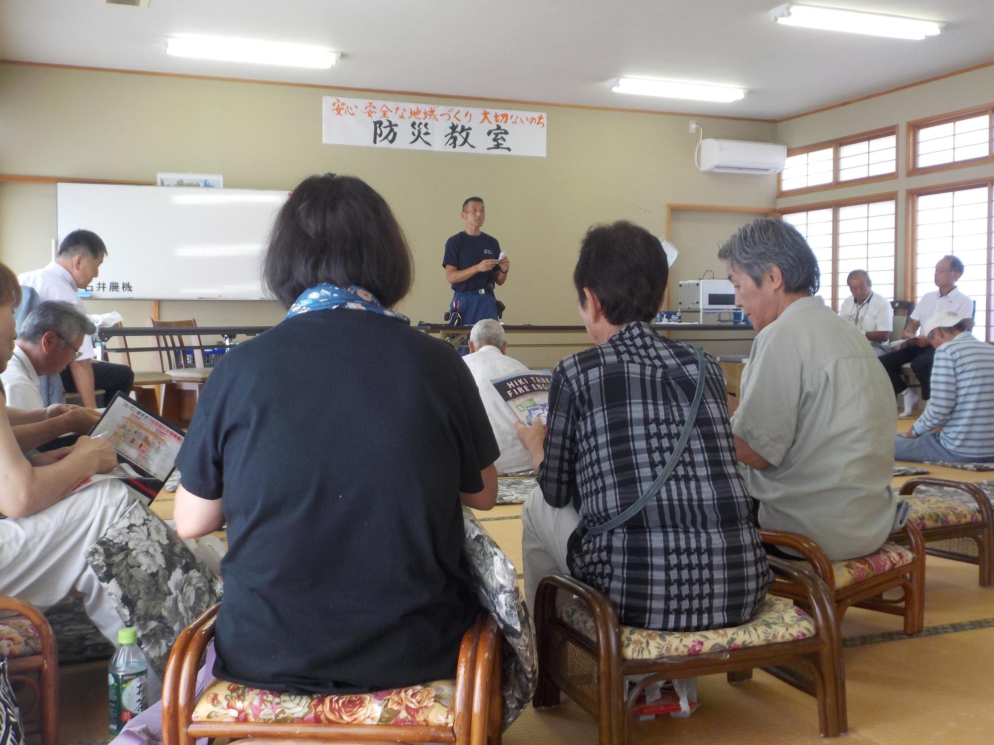 参加者達が背の低い椅子に腰かけ、室内前方で話をしている消防署員の方の話を真剣に聞いている様子の写真