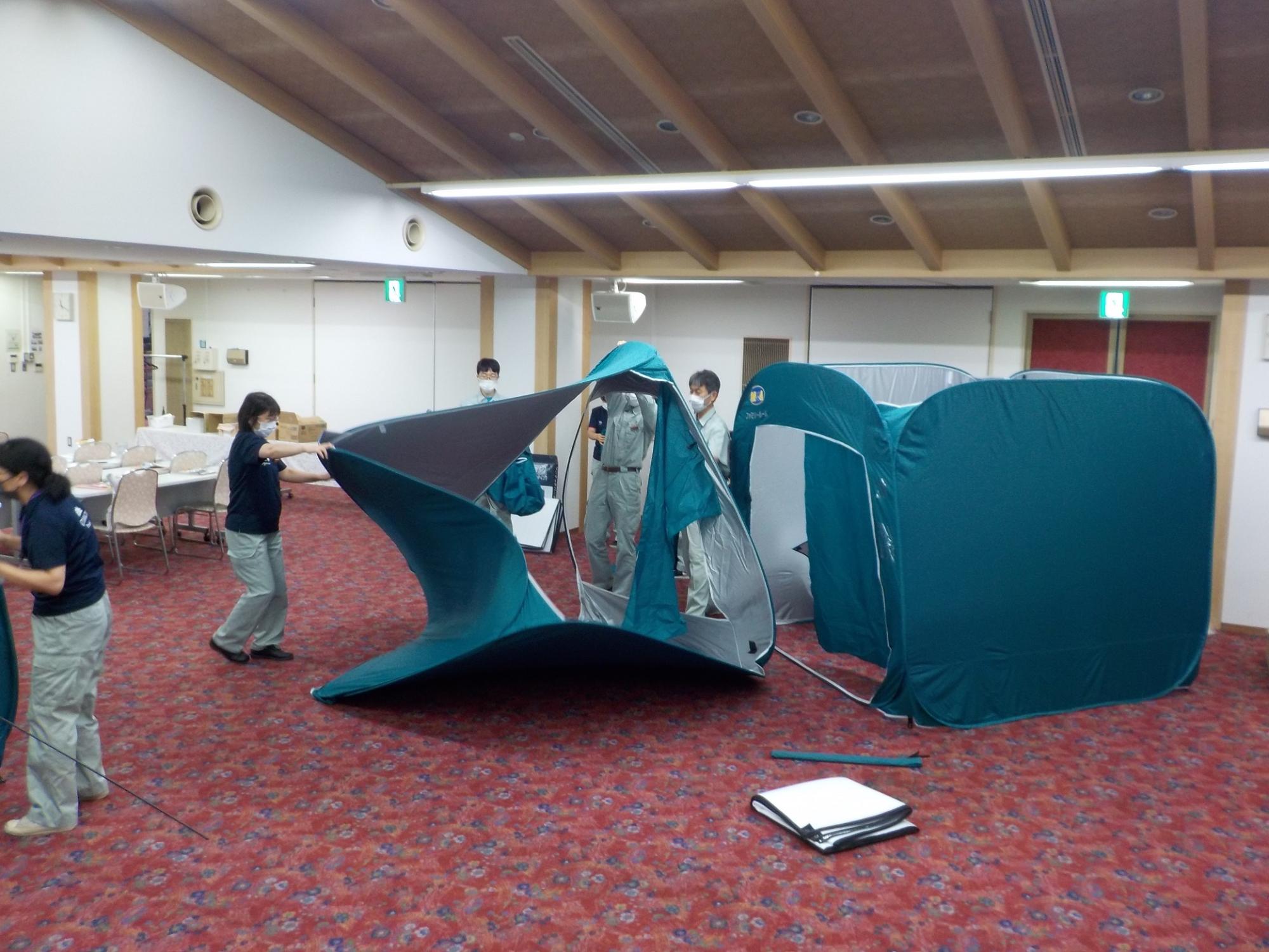 訓練の参加者たちが広い会議室の中でプライベートルームとして使えるテントを組み立てている写真
