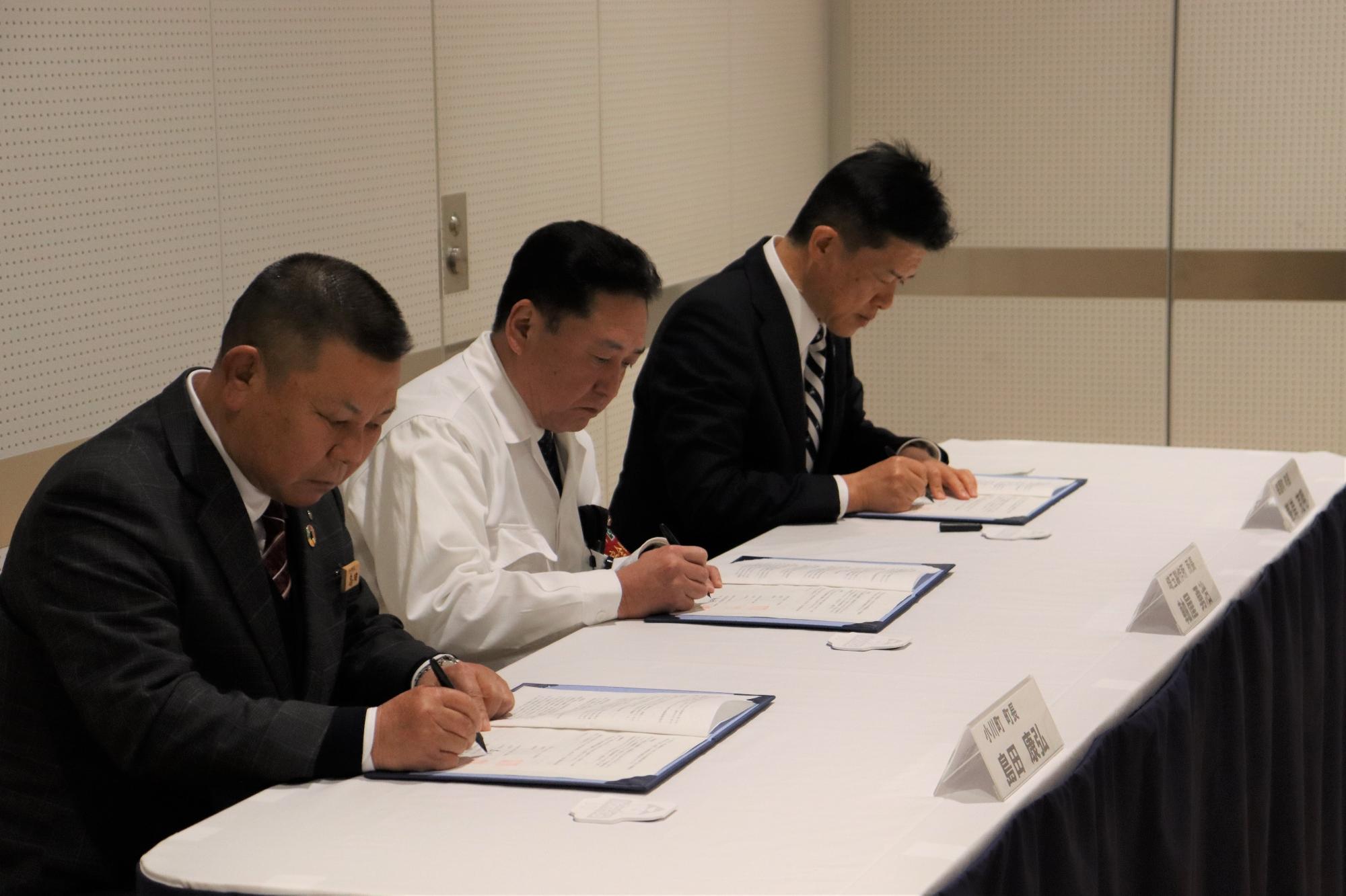 長机に3名の方が座り調印を行っている様子を斜め前から写した写真