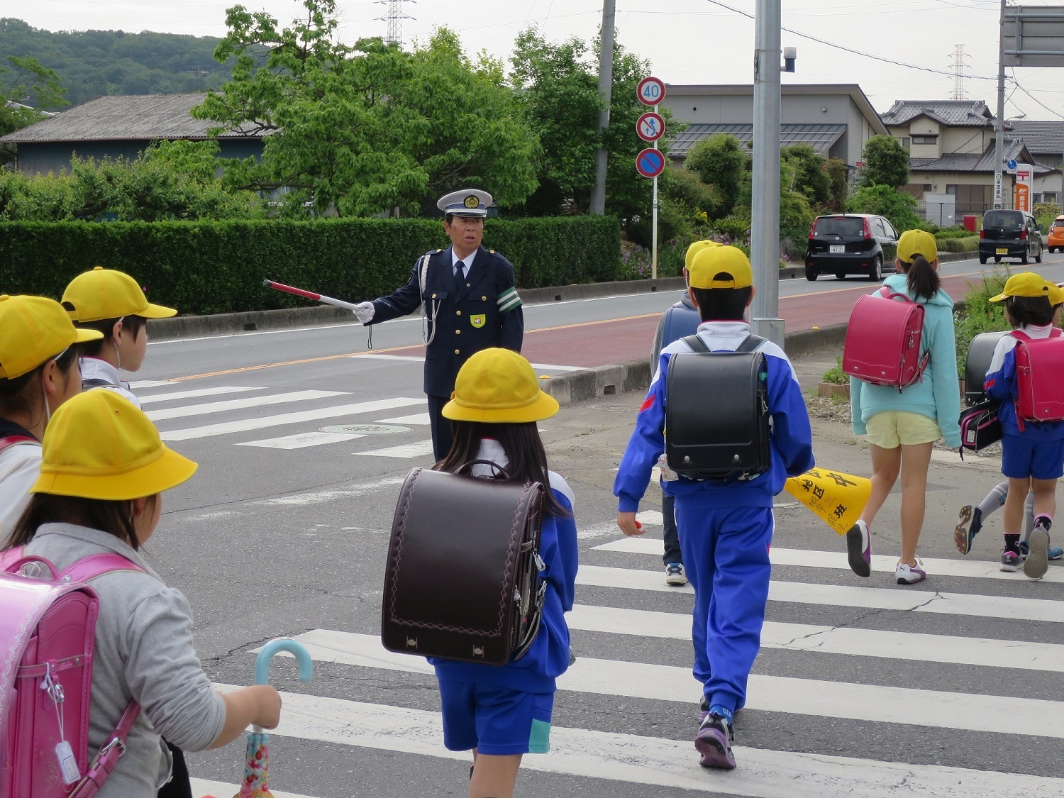 制服姿の交通安全隊員の男性が横断歩道を渡る小学生たちの安全を守っている写真