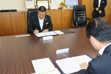 島田町長と梅木代表理事が向かい合わせに座りながら調印書にサインをしている写真