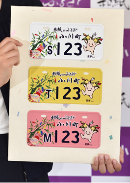 上から白、黄色、ピンクの三種類の「和紙のふるさと小川町」とかかれ星夢ちゃんのイラストが描かれたナンバープレートが並んでいる写真