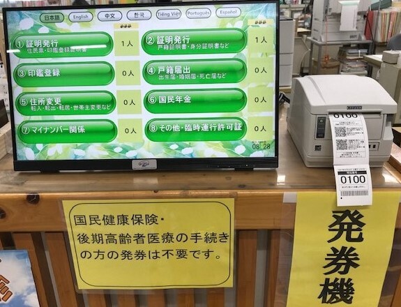 左側の「国民健康保険・後期高齢者医療の手続きの方の発券は不要です。」と書かれたカウンターにタッチパネルが設置され、右側の「発券機」と書かれたカウンターに2枚の呼出し番号札が排出された発券機が置かれている写真