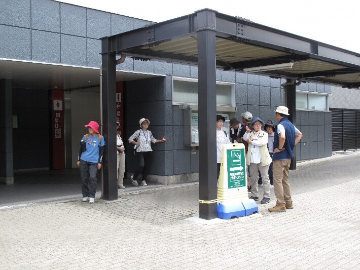 参加者たちが柱と屋根だけで作られた建物の下で話をしている写真