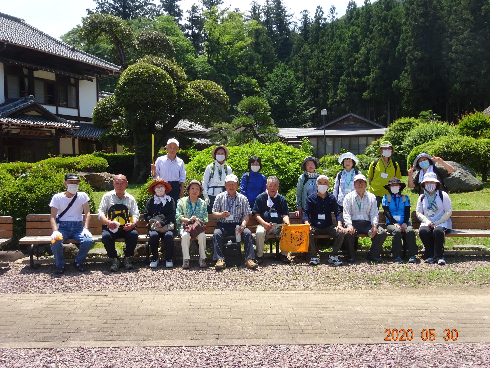 強い日差しの下、青々とした木々を背景に東秩父和紙の里で2列に並んだ参加者の方々を撮影した集合写真