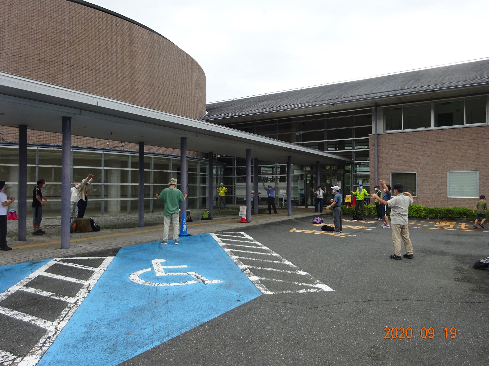 曇り空の下、建物の前で参加者の方々が準備運動をしている様子の写真