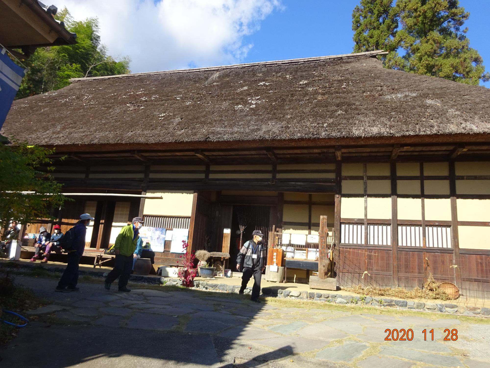 茅葺屋根の吉田家住宅で縁側に座ったり立って話しながら休憩をとる参加者の様子を前方から撮影した写真