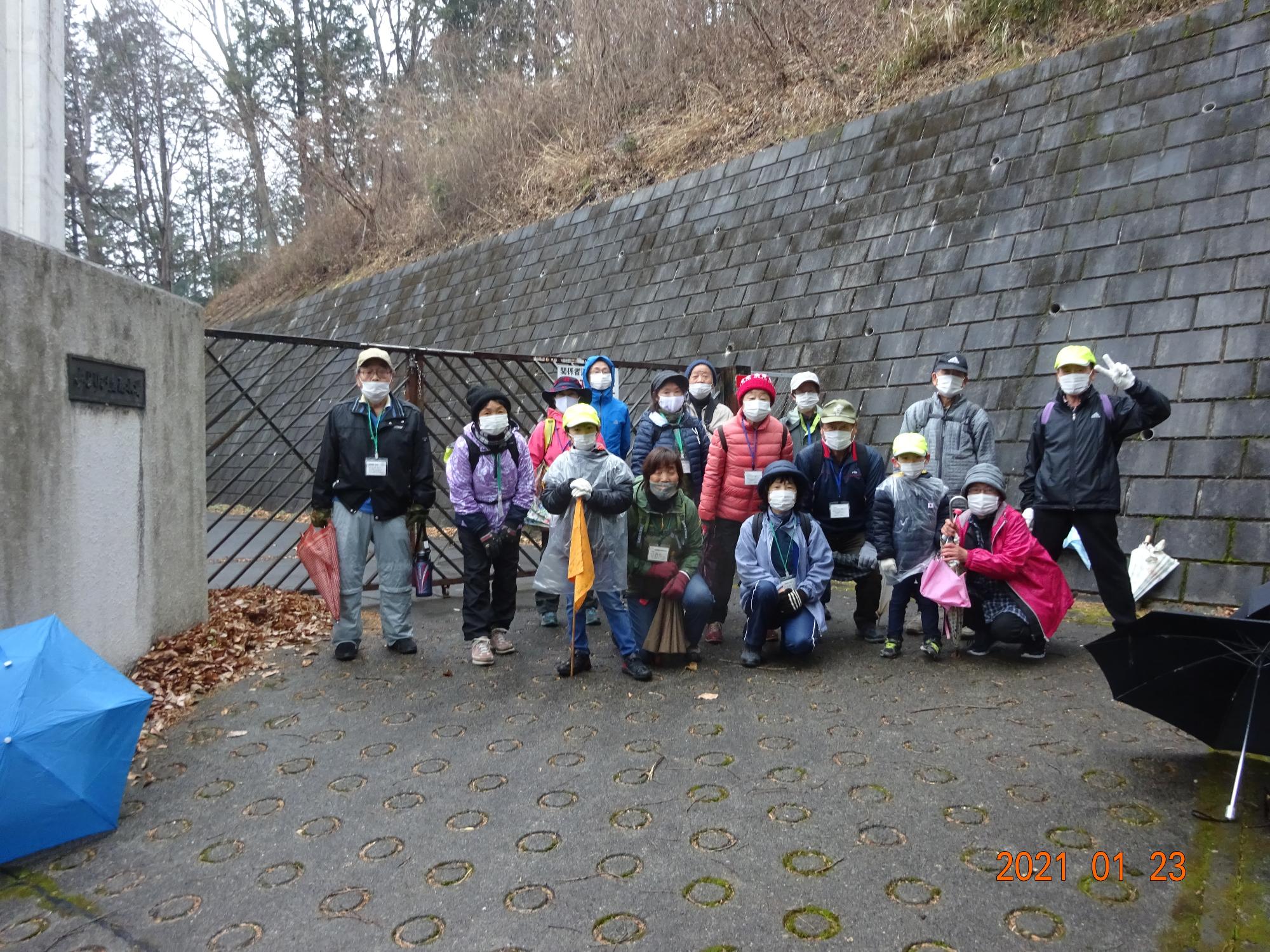傘を片手に3列に並んだ参加者の方々が貯水場付近で撮影した集合写真