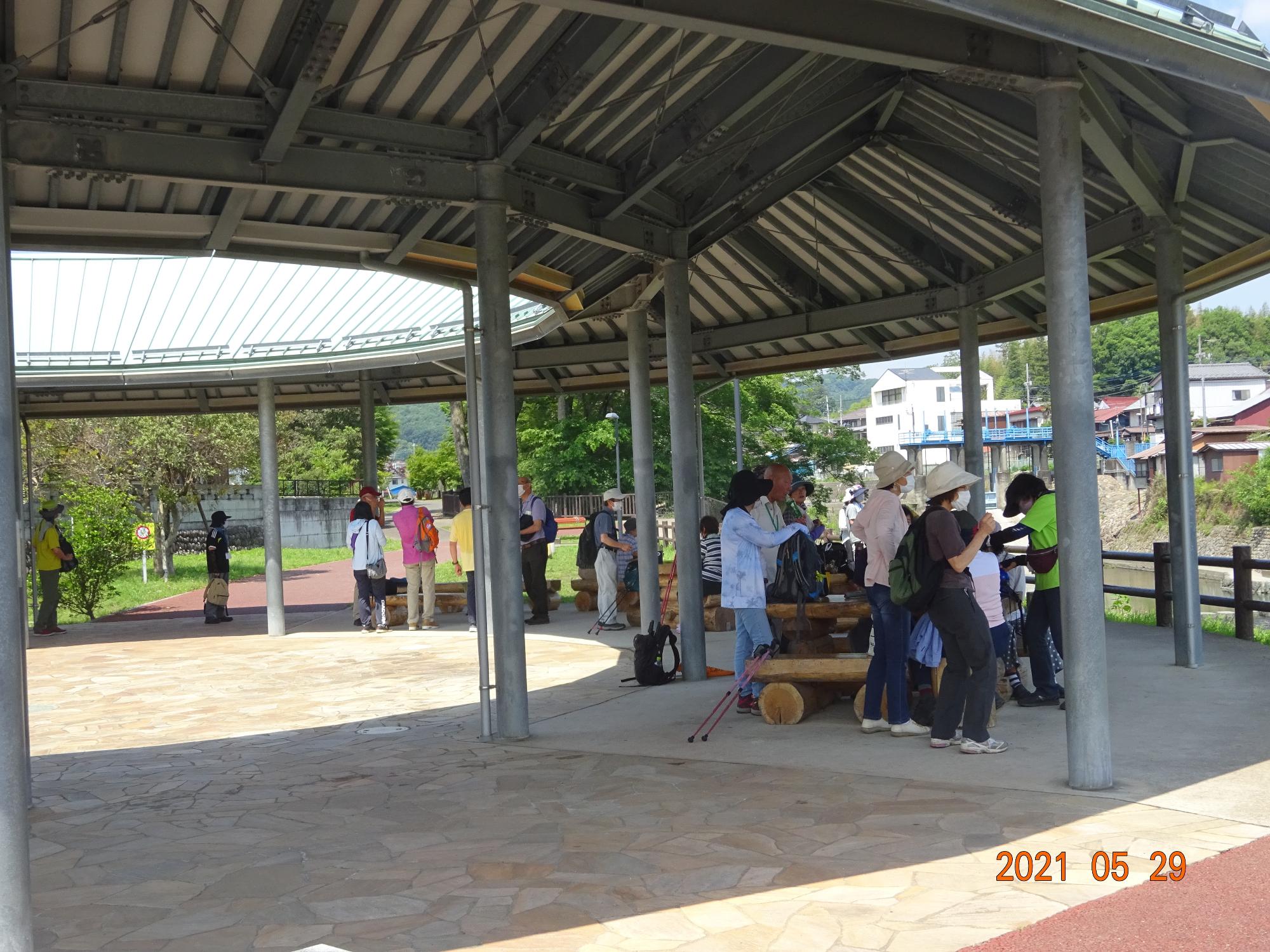 参加者たちが栃本親水公園の中にある屋根と柱だけの建物の下で休憩をしている写真