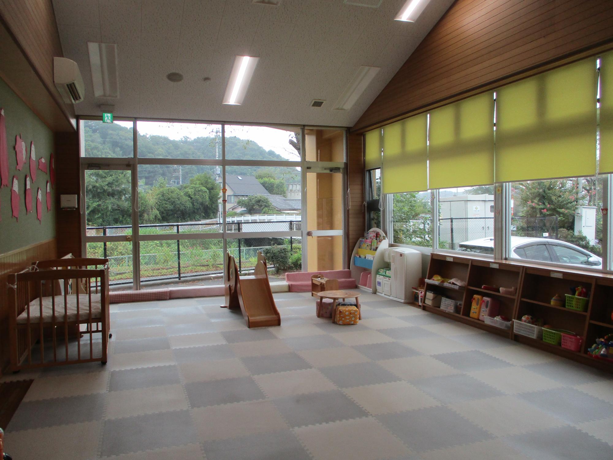 窓下の棚の壁に消防車やパトカーなどのイラストが貼られ、貼られた場所におもちゃが置かれている写真